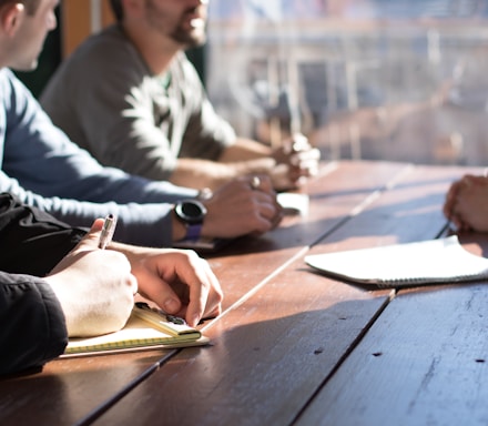 people sitting on chair in front of table while holding pens during daytime