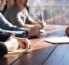 people sitting on chair in front of table while holding pens during daytime