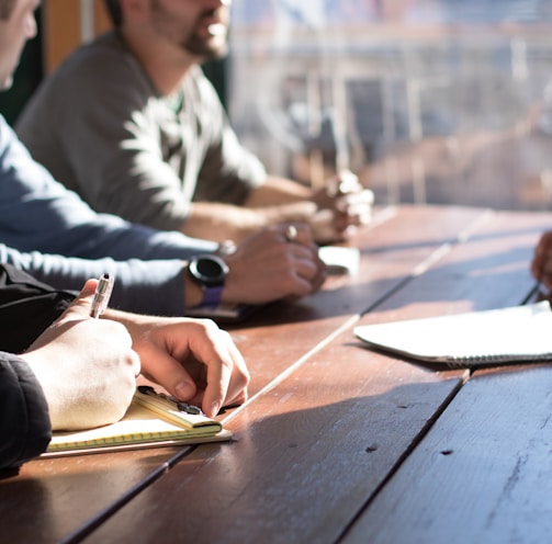 people sitting on chair in front of table while holding pens during daytime