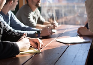 people sitting on chair in front of table while holding pens during daytime