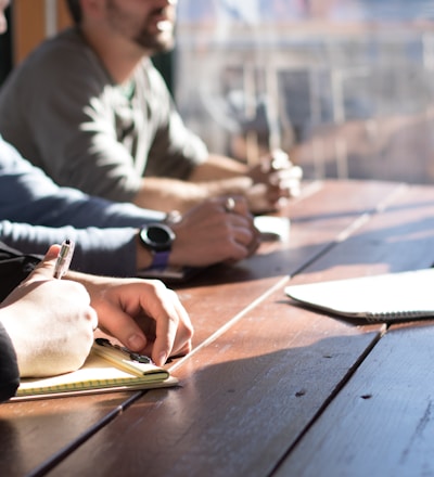 people sitting on chair in front of table while holding pens during daytime