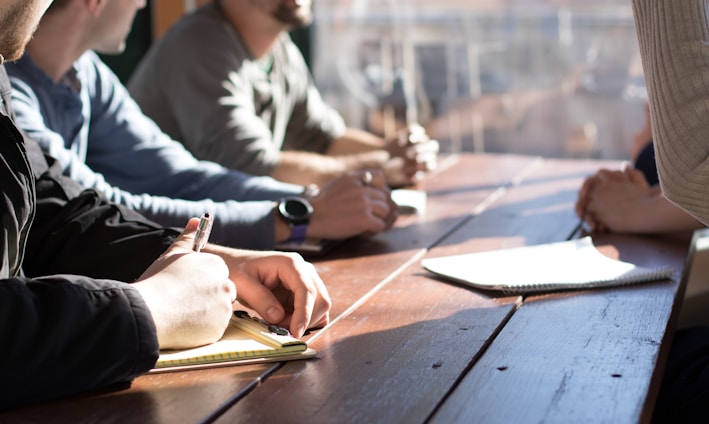 people sitting on chair in front of table while holding pens during daytime