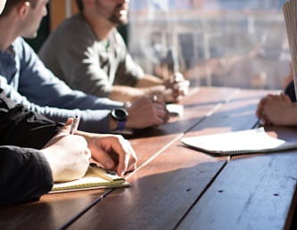 people sitting on chair in front of table while holding pens during daytime