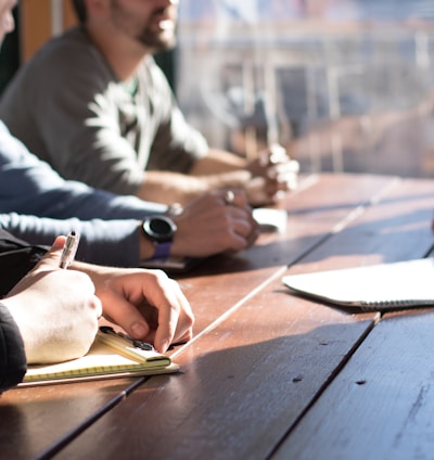 people sitting on chair in front of table while holding pens during daytime