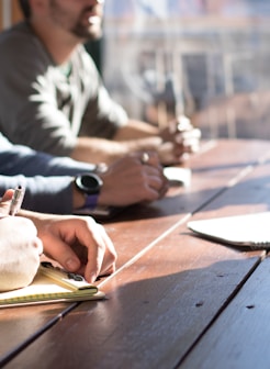 people sitting on chair in front of table while holding pens during daytime