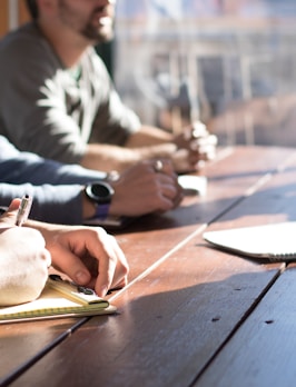 people sitting on chair in front of table while holding pens during daytime