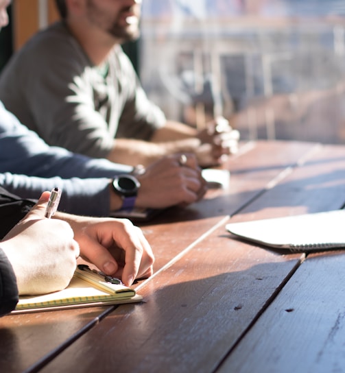 people sitting on chair in front of table while holding pens during daytime