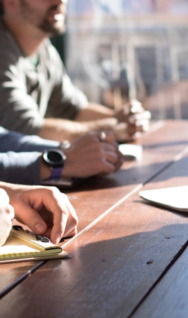 people sitting on chair in front of table while holding pens during daytime