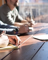 people sitting on chair in front of table while holding pens during daytime