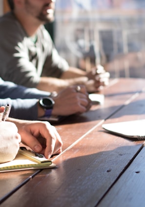 people sitting on chair in front of table while holding pens during daytime