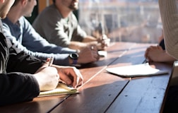 people sitting on chair in front of table while holding pens during daytime