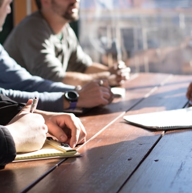 people sitting on chair in front of table while holding pens during daytime