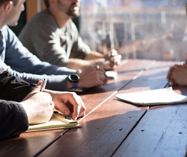 people sitting on chair in front of table while holding pens during daytime