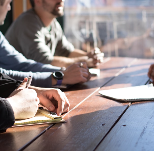 people sitting on chair in front of table while holding pens during daytime