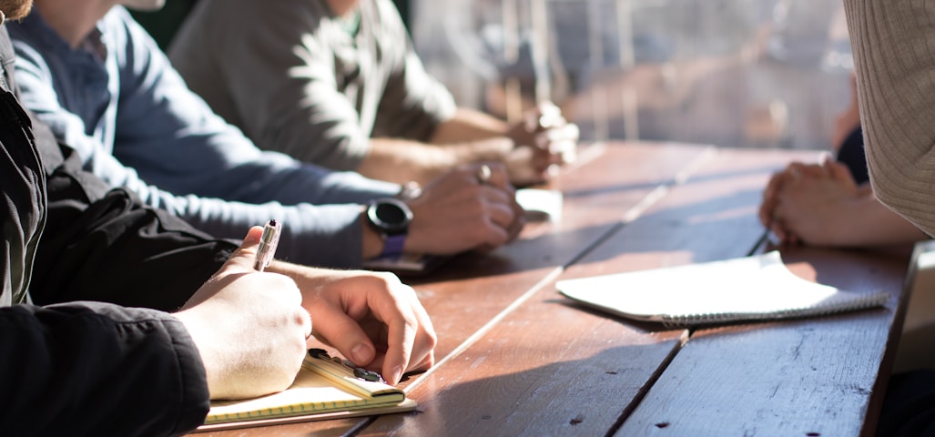 people sitting on chair in front of table while holding pens during daytime