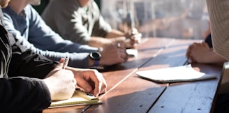 people sitting on chair in front of table while holding pens during daytime