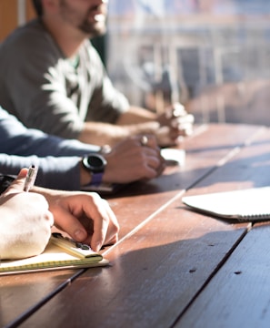 people sitting on chair in front of table while holding pens during daytime