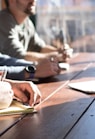 people sitting on chair in front of table while holding pens during daytime