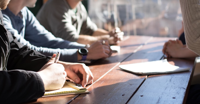 people sitting on chair in front of table while holding pens during daytime