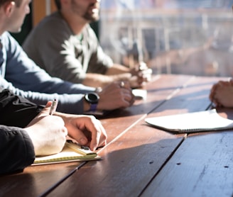 people sitting on chair in front of table while holding pens during daytime