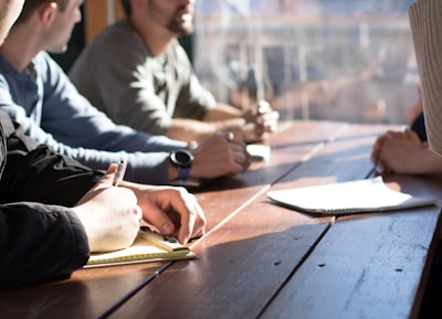 people sitting on chair in front of table while holding pens during daytime