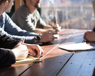 people sitting on chair in front of table while holding pens during daytime