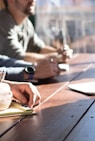 people sitting on chair in front of table while holding pens during daytime