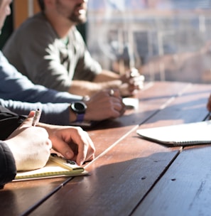 people sitting on chair in front of table while holding pens during daytime