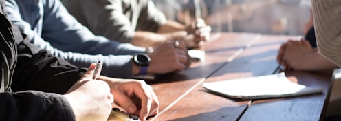 people sitting on chair in front of table while holding pens during daytime