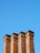 Four tall brick chimneys rise against a clear blue sky. Each chimney is uniformly constructed with red bricks, showing detailed brick patterns and slight weathering.