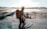 man in black top standing in front of sun holding selfie stick