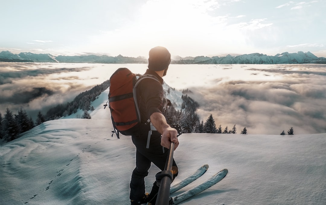 man in black top standing in front of sun holding selfie stick, Above the Clouds