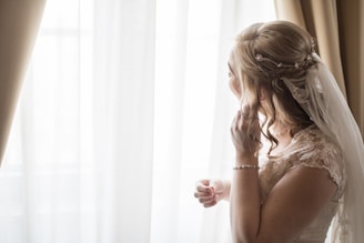 woman wearing white bridal gown near window curtain