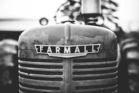 Close-up image of a mechanic inspecting a tractor engine outdoors on a farm.