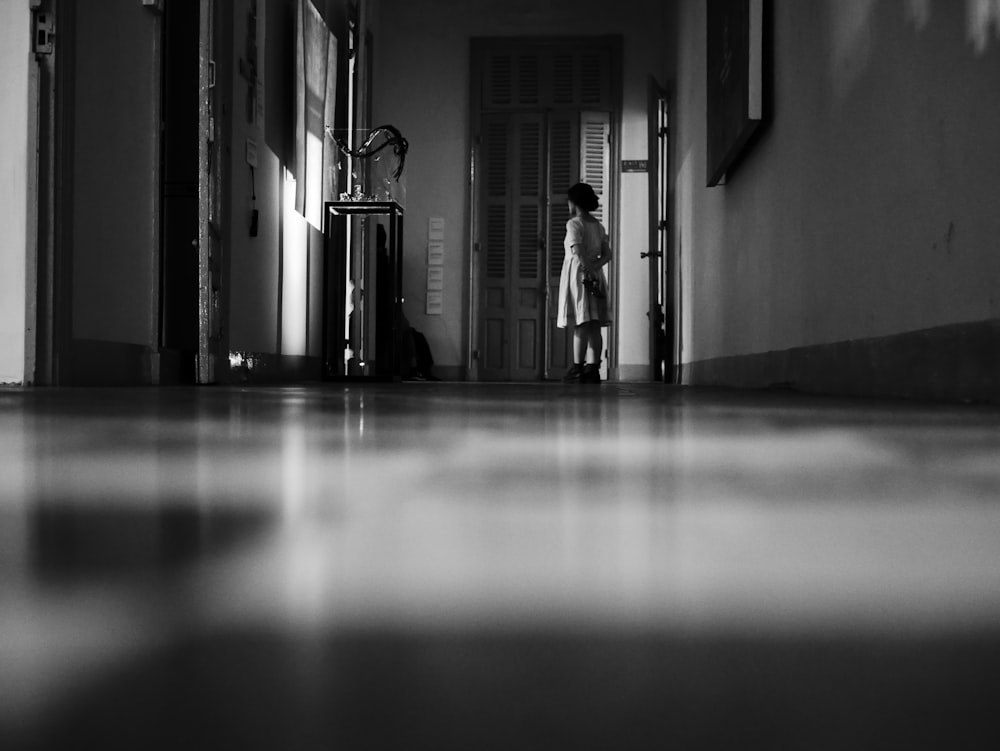 grayscale photo of woman standing near wall and open door