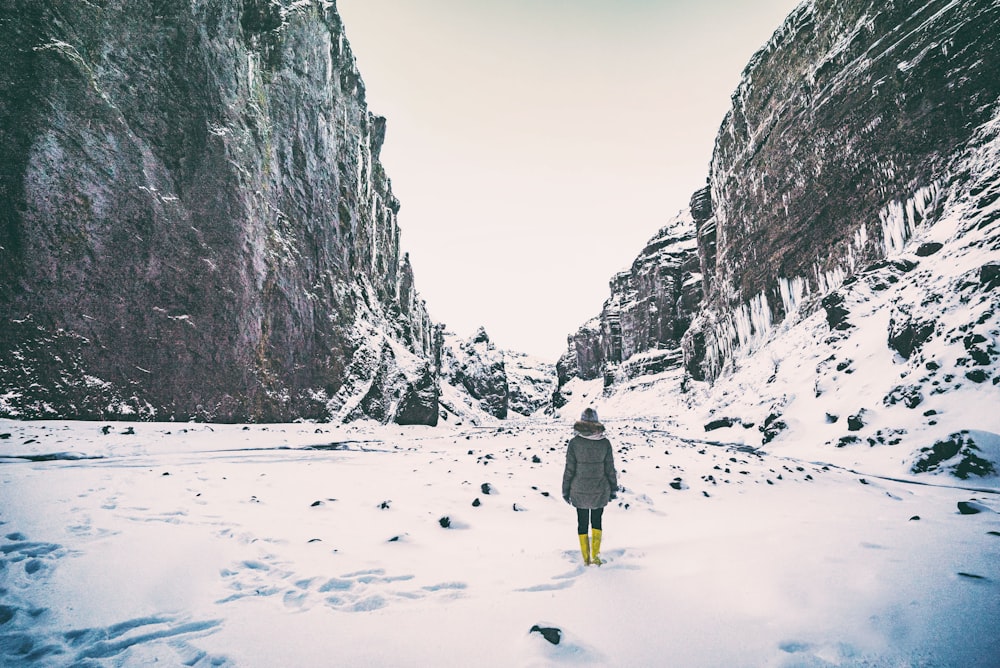 Mujer con abrigo gris de pie en medio de la montaña cubierta de nieve