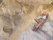 A scene in a quarry with large piles of sand and gravel. Heavy machinery, including trucks and conveyor belts, is visible, indicating active work in the extraction process.