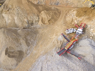 A scene in a quarry with large piles of sand and gravel. Heavy machinery, including trucks and conveyor belts, is visible, indicating active work in the extraction process.