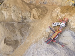 A scene in a quarry with large piles of sand and gravel. Heavy machinery, including trucks and conveyor belts, is visible, indicating active work in the extraction process.