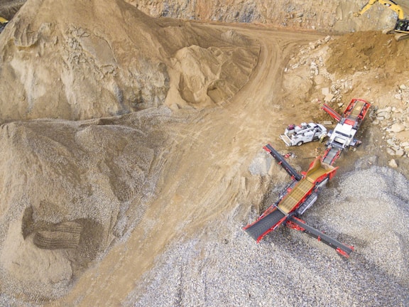 A scene in a quarry with large piles of sand and gravel. Heavy machinery, including trucks and conveyor belts, is visible, indicating active work in the extraction process.