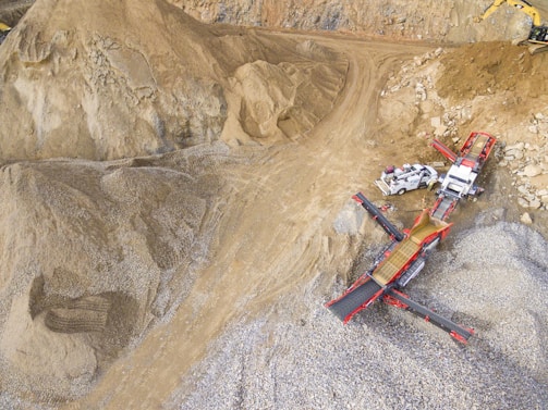 A scene in a quarry with large piles of sand and gravel. Heavy machinery, including trucks and conveyor belts, is visible, indicating active work in the extraction process.