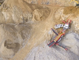 A scene in a quarry with large piles of sand and gravel. Heavy machinery, including trucks and conveyor belts, is visible, indicating active work in the extraction process.