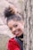 woman wearing black and red blazer hiding behind tall tree while smiling during daytime