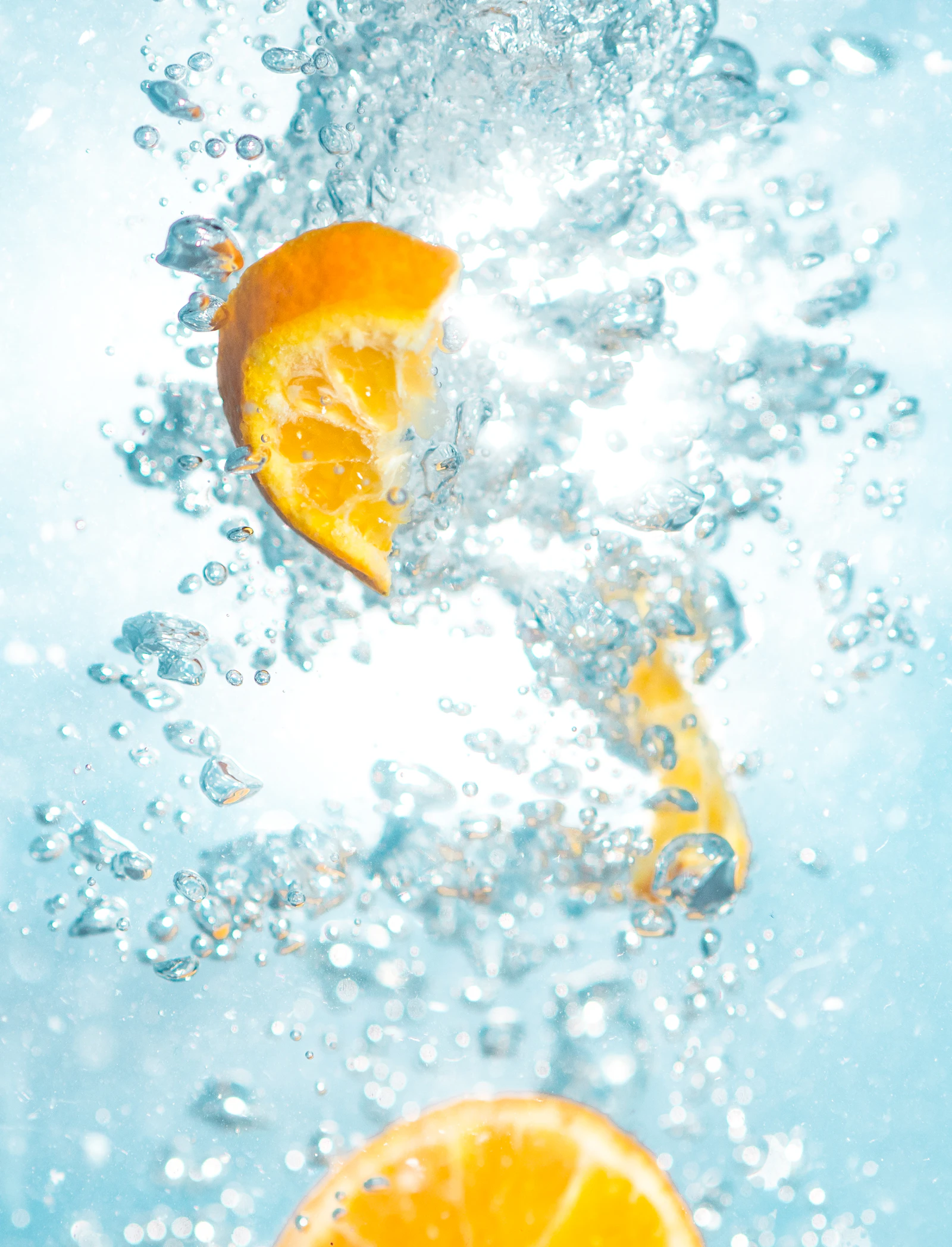 Slices of orange dropping through clear sparkling water with bubbles rising around them.
