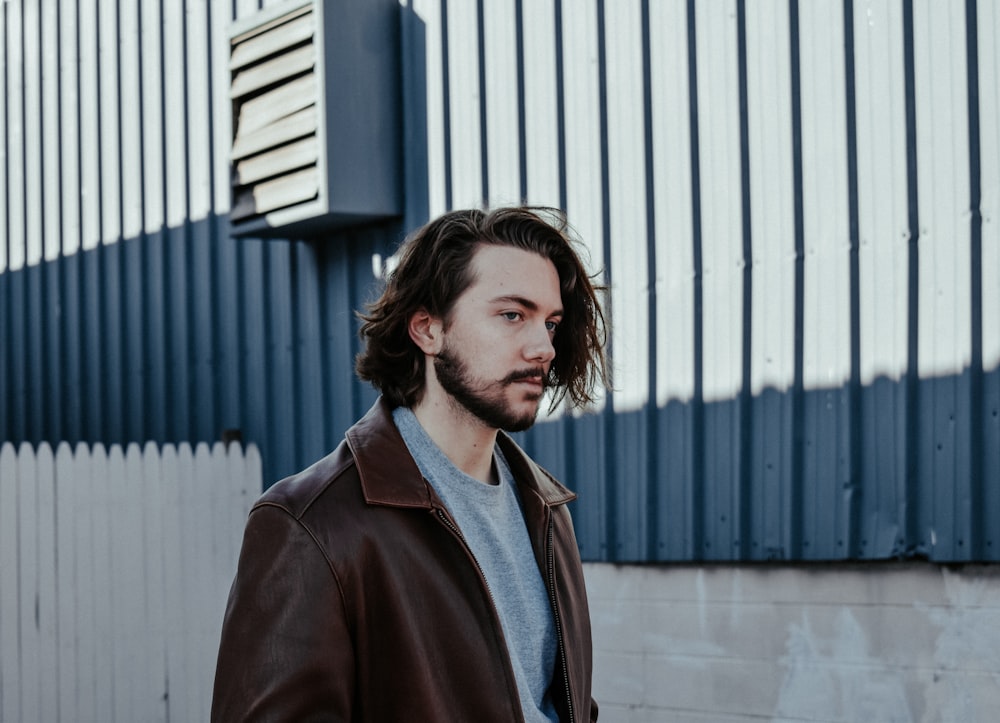 man wearing brown leather jacket standing against grey background