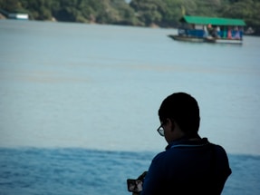 A friendly person holding a phone near Torch Lake with boats in the background.