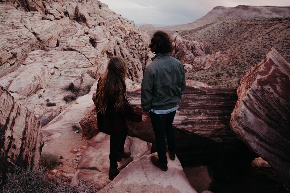 man and woman standing on hill in front of hills during daytime