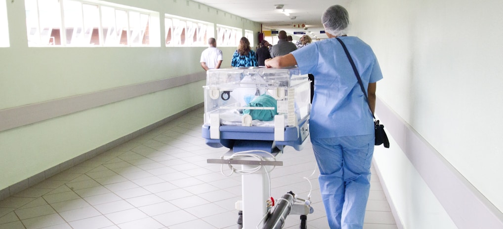 person walking on hallway in blue scrub suit near incubator