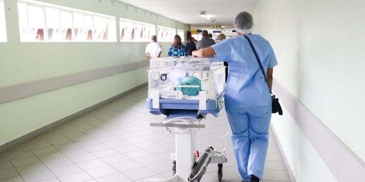 person walking on hallway in blue scrub suit near incubator