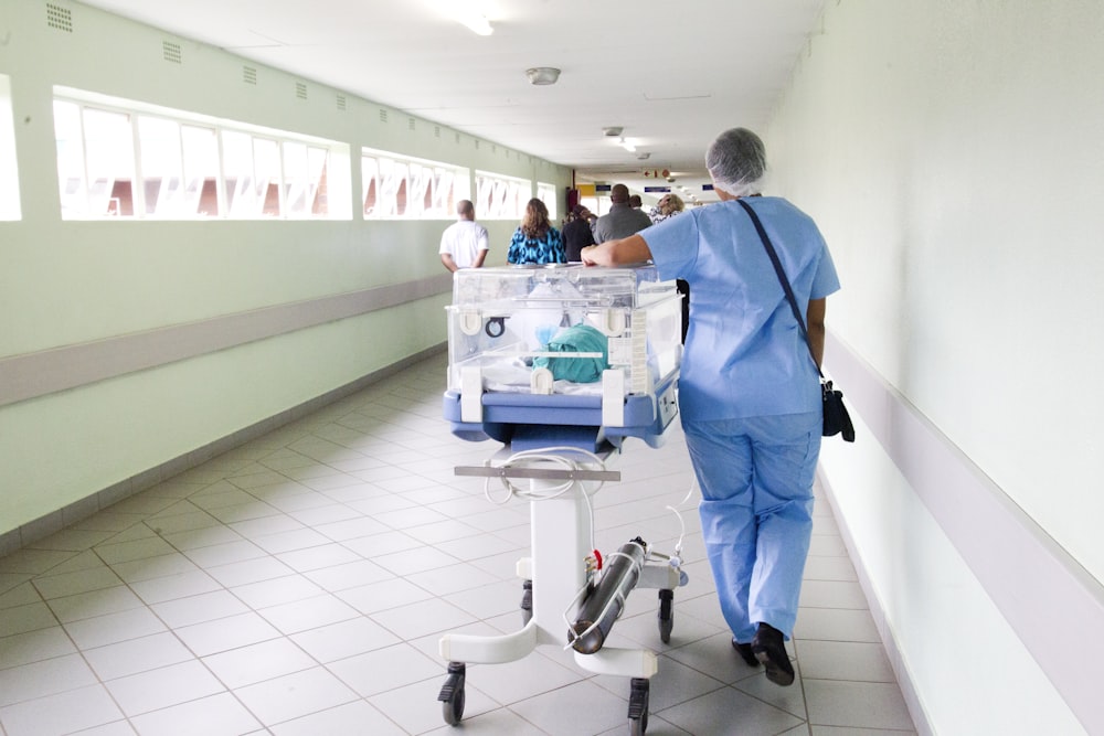 person walking on hallway in blue scrub suit near incubator